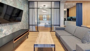 Ein modernes Wohnzimmer mit Fernseher, Sofa, Couchtisch und Blick ins Schlafzimmer.