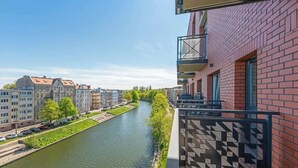 A river with buildings on one side and a red brick building with a patterned balcony on the other.