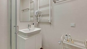 A bathroom with a white sink, mirror, towel rack, and a shelf with toiletries.