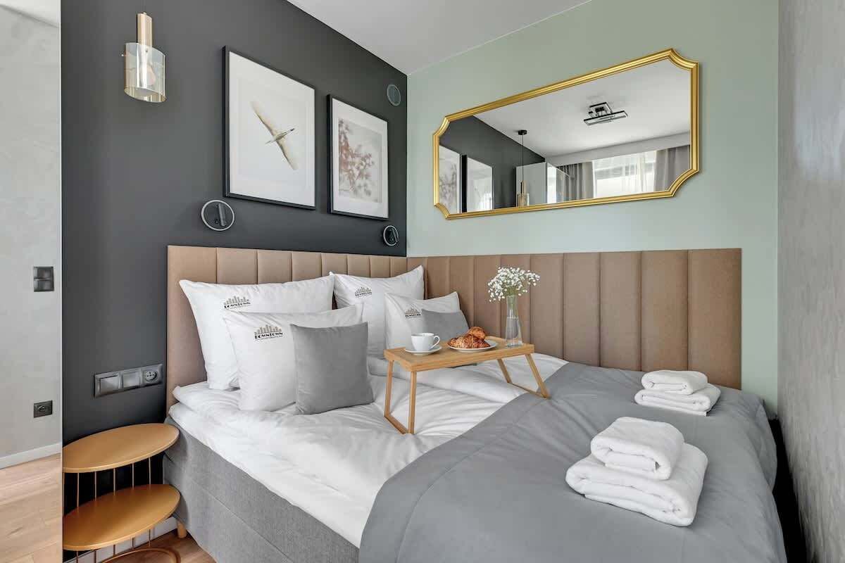 Una habitación de hotel moderna con una cama grande, una mesita de noche con una bandeja de desayuno, un espejo redondo y obras de arte en las paredes.