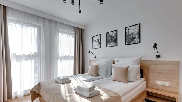 A modern hotel room with a large bed, a bedside table, a desk, and a window with curtains. - Grano Residence 112 | Riverside | Parking (Gdańsk)