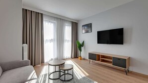 A modern living room with a sofa, two small tables, a TV, and a plant. - Grano Residence 112 | Riverside | Parking (Gdańsk)