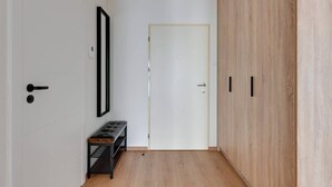 A hallway with a white door, a bench, and a wardrobe with a light wood finish. - Grano Residence 112 | Riverside | Parking (Gdańsk)