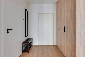 A hallway with a white door, a bench, and a wardrobe with a light wood finish. - Grano Residence 112 | Riverside | Parking (Gdańsk)