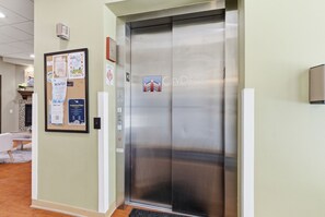 A modern elevator with a metallic finish, a bulletin board with various notices, and a 'CityDeck Landing' sign.