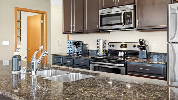 A modern kitchen with granite countertops, stainless steel appliances, and dark wooden cabinets. - Riverfront Retreat – 10 Mins to Lambeau! (Green Bay)