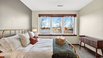 A bedroom with a bed, a bedside table, a lamp, a window with a view, and a bench.