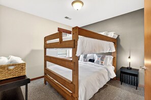 A bunk bed with white bedding, a wicker basket on a nightstand, and a bedside lamp.