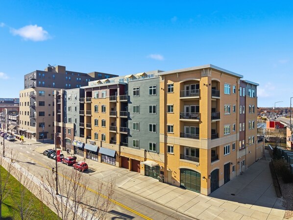 A multi-story building with a ground-level commercial space, a parking lot, and a clear sky.