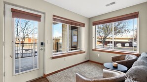A room with a sliding glass door, a window with a view of a building, a brown leather sofa, and a small round table. - Riverfront Retreat – 10 Mins to Lambeau! (Green Bay)