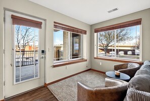 Ein Zimmer mit Schiebetür, Fenster mit Blick auf ein Gebäude, ein braunes Ledersofa und ein kleiner runder Tisch.