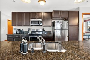 A modern kitchen with dark brown cabinets, stainless steel appliances, granite countertops, and a double sink.