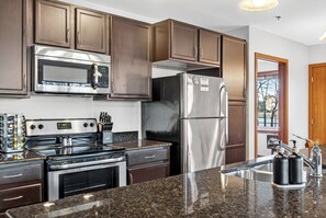 A kitchen with stainless steel appliances, dark wooden cabinets, granite countertops, and a window with a view. - Riverfront Retreat – 10 Mins to Lambeau! (Green Bay)