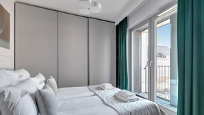 A modern hotel room with a bed, a wardrobe, and a balcony with curtains. - Grano Residence 64 with Balcony | Riverside (Gdańsk)