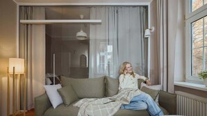 Ein Zimmer mit einer Couch, einer Lampe und einem Fenster mit Vorhängen.