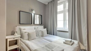 Ein ordentlich eingerichtetes Schlafzimmer mit Bett, Nachttischen, einer Lampe und einem Fenster mit Vorhängen.