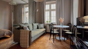 Ein modernes Wohnzimmer mit einer Couch, einem Esstisch, Stühlen, einem Klavier und großen Fenstern mit Vorhängen.