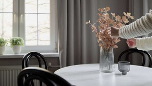 Ein Esstisch mit einer Blumenvase, einer Glasgießkanne und einer Metalltasse.