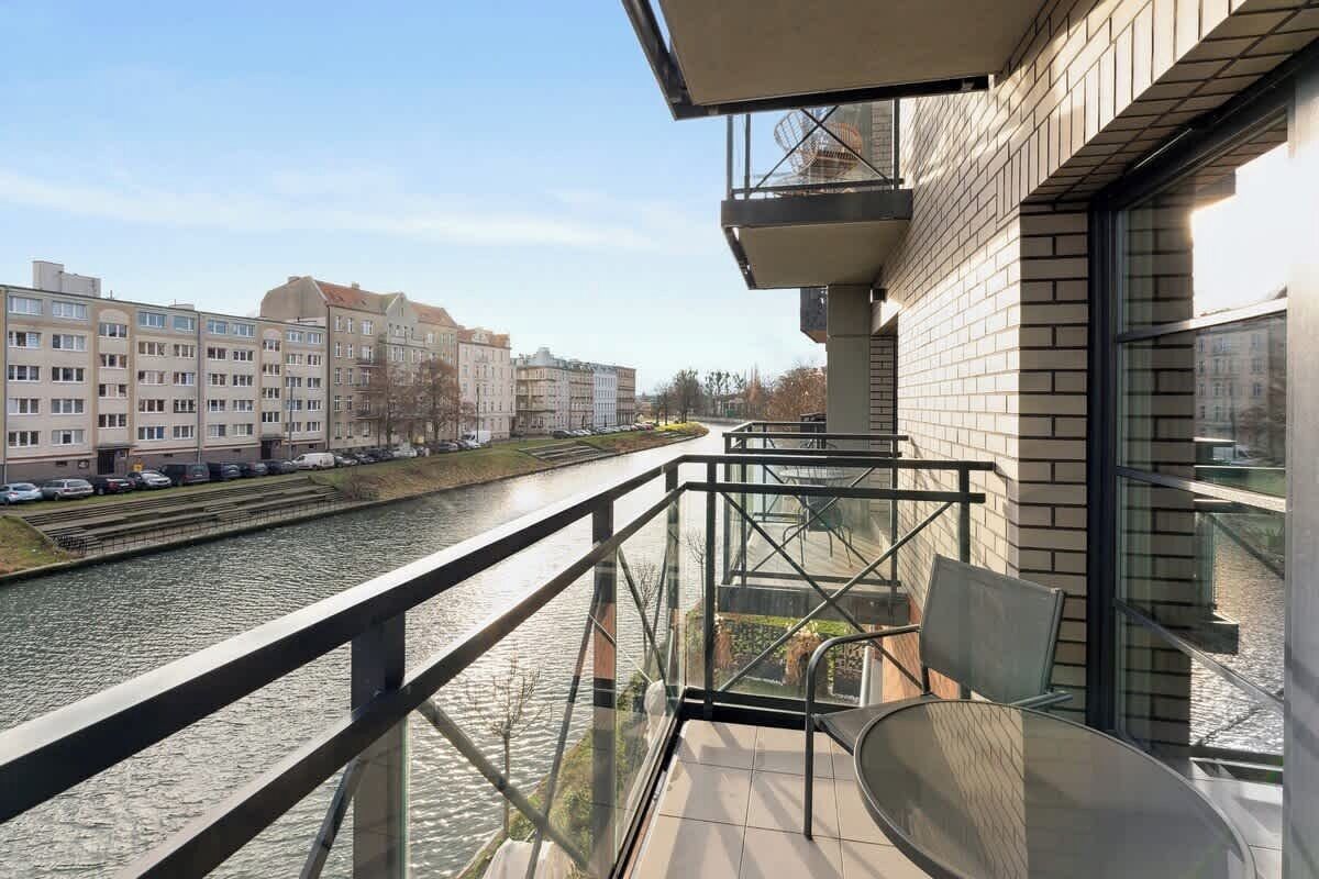 Un balcon doté d’une balustrade en verre donnant sur une rivière, avec une table et des chaises.