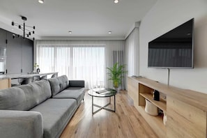 Una sala de estar moderna con un sofá, una mesa de centro, un televisor y una cocina al fondo.