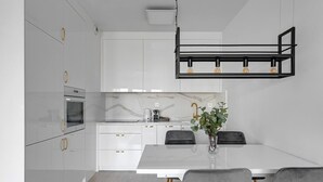 A modern kitchen with white cabinetry, a marble countertop, a built-in oven, and a pendant light fixture. - Grano Residence 114 with Balcony | Riverside (Gdańsk)