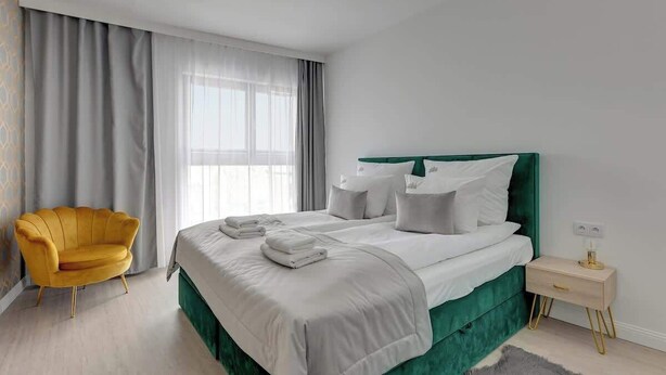 A modern hotel room with a large bed, a yellow armchair, and a bedside table. - Grano Residence 114 with Balcony | Riverside (Gdańsk)
