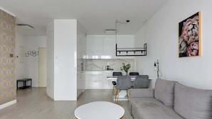 A modern living room with a grey sofa, a round white coffee table, and a dining area with a white table and chairs. - Grano Residence 114 with Balcony | Riverside (Gdańsk)