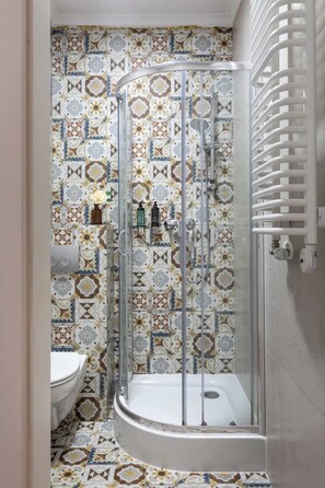Um chuveiro com porta de vidro, vaso sanitário e azulejos estampados.