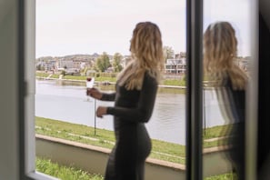Eine Person steht an einem Fenster mit Blick auf einen Fluss und Gebäude im Hintergrund.