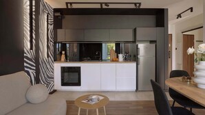 A modern kitchen with a built-in oven, a refrigerator, and a dining area with a wooden table and chairs. - Vistula View - Riva Verona | Parking (Kraków)