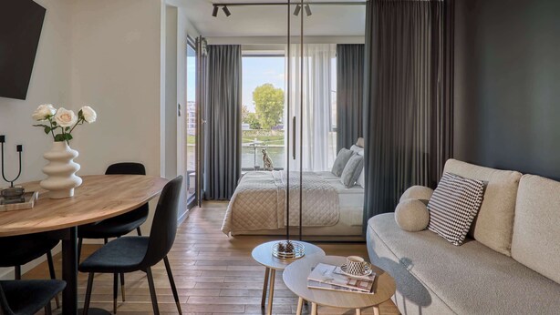 A modern room with a dining table, chairs, a sofa, a small coffee table, and a bed with a view. - Vistula View - Riva Verona | Parking (Kraków)
