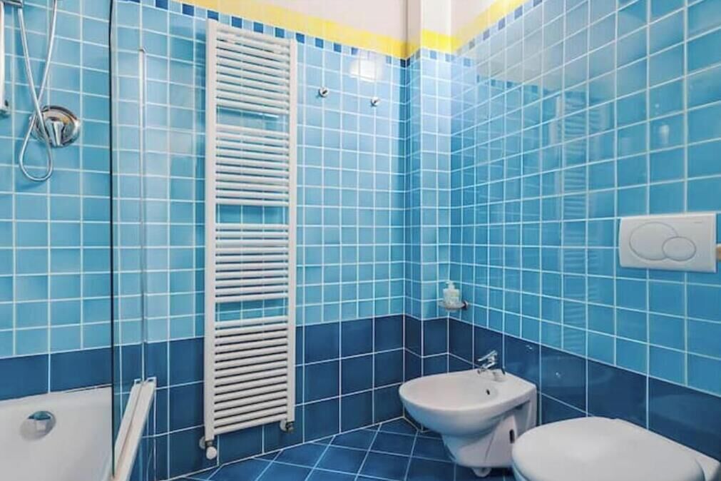 A bathroom with blue tiles, a white radiator, a toilet, and a bidet.