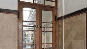 Eine Holztür mit doppelten Flügeln und Glasfeldern, ein Betonboden mit geometrischem Muster und eine schlichte Wand.