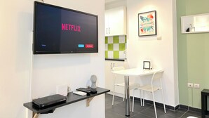 A modern room with a flat-screen TV displaying the Netflix logo, a small table with a chair, a decorative bust, and a framed artwork on the wall. - Cozy Studio Near City Center I Walk to Metro (Athina)