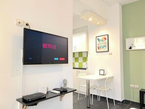 A modern room with a flat-screen TV displaying the Netflix logo, a small table with a chair, a decorative bust, and a framed artwork on the wall. - Cozy Studio Near City Center I Walk to Metro (Athina)