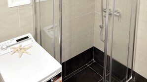 A shower with a glass door, a window with blinds, and a control panel with a starfish decoration. - Cozy Studio Near City Center I Walk to Metro (Athina)