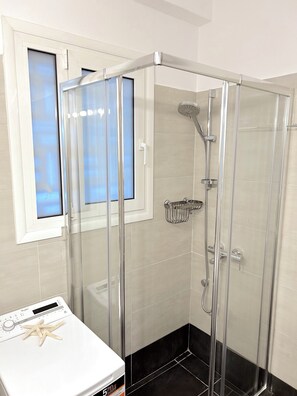 A shower with a glass door, a window with blinds, and a control panel with a starfish decoration. - Cozy Studio Near City Center I Walk to Metro (Athina)