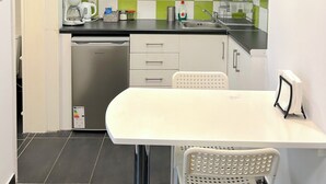 A compact kitchen with white cabinets, a green and white checkered backsplash, a stainless steel dishwasher, and a white table with a chair. - Cozy Studio Near City Center I Walk to Metro (Athina)