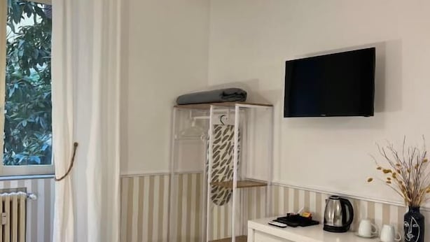 A room with a bed, a desk, a TV, a radiator, and a window with curtains.