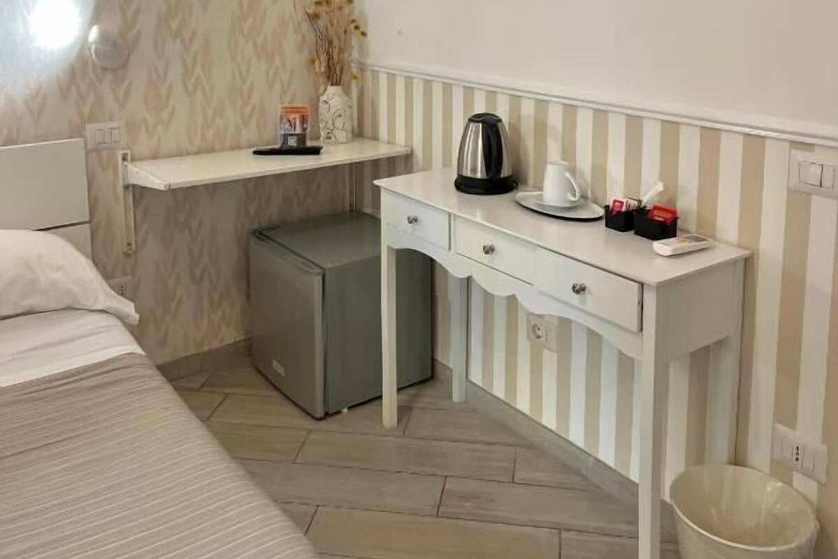 Una habitación de hotel pequeña con cama, escritorio con tetera, televisión y radiador.