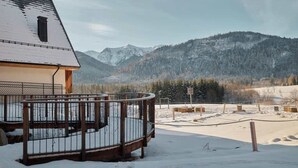 En byggnad med ett snötäckt tak, en balkong med ett metallräcke och en utsikt över snöklädda berg i bakgrunden.