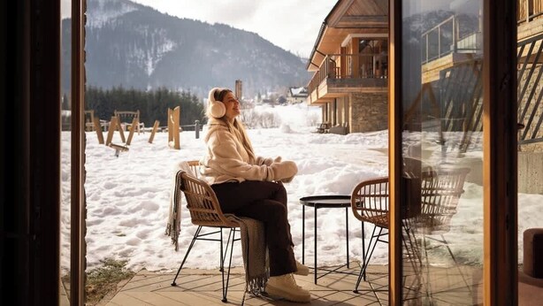 En person sitter vid ett fönster och blickar ut över ett snötäckt landskap med berg i fjärran.