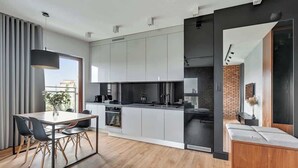 A modern kitchen with grey cabinets, a dining area with a wooden table and chairs, and a built-in bench with a cushioned seat. - Nowa Motława 32.1 | River View | SPA & Parking (Gdańsk)