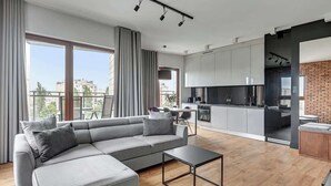 A modern apartment with a grey sectional sofa, a small black coffee table, a kitchen with grey cabinets, and a brick accent wall. - Nowa Motława 32.1 | River View | SPA & Parking (Gdańsk)