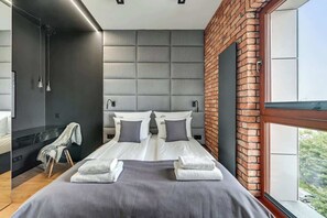 Ein modernes Hotelzimmer mit einem großen Bett, einer Wand aus Ziegelsteinen, einem großen Fenster und einer Duschkabine.