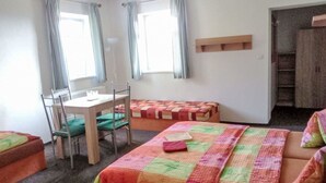 Ein Zimmer mit einem Bett, einem Schreibtisch und einem Stuhl. Zwei Fenster mit Vorhängen sind vorhanden.