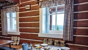 Ein Essbereich im Holzblockhaus-Stil mit karierten Vorhängen, einem gedeckten Tisch mit Tellern, Brot und Beilagen.