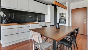 A modern kitchen with white cabinets, a wooden countertop, and a dining area with a large table and chairs. - Aura 29 | Riverside | City Center (Gdańsk)