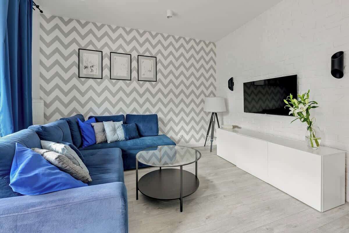 A modern living room with a blue sofa, a glass coffee table, a white cabinet, and a TV mounted on the wall.