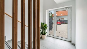 Un interior moderno con barandilla de madera, una planta en maceta y vista a un coche rojo fuera a través de una puerta de cristal.